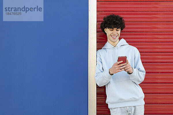 Glücklicher Mann mit Smartphone  der vor einer zweifarbigen Wand steht