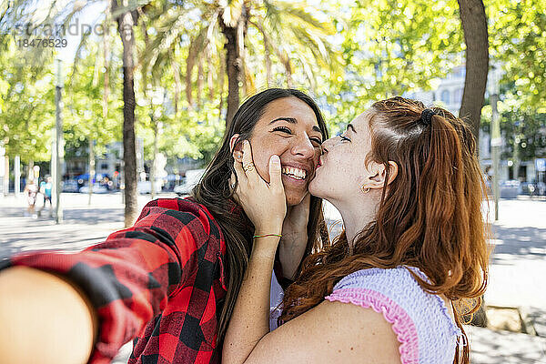 Frau küsst Freundin und macht Selfie auf Fußweg