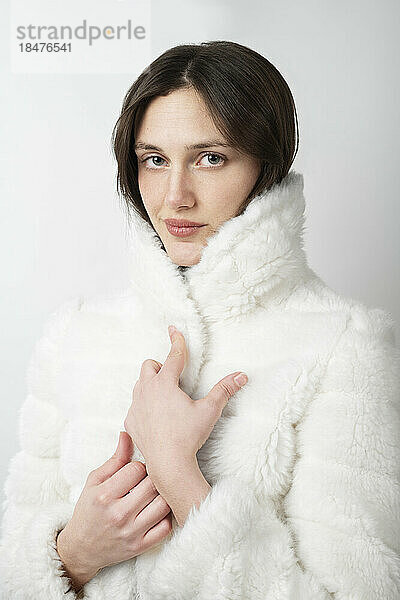 Young woman wearing fur coat against white background