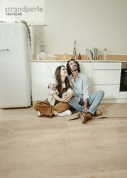 Glückliches Paar sitzt mit gekreuzten Beinen auf dem Boden und träumt in der Küche