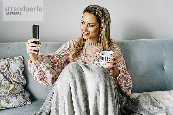 Lächelnde junge Frau  die zu Hause auf dem Sofa ein Selfie mit dem Smartphone macht