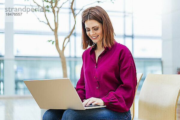 Lächelnde Geschäftsfrau  die Laptop auf Stuhl benutzt
