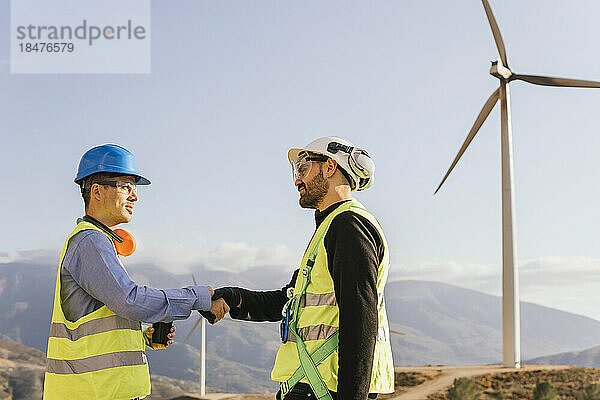 Ingenieur schüttelt Techniker vor Windkraftanlagen die Hand