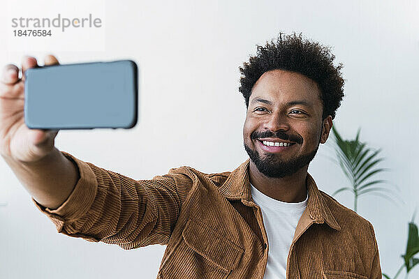Glücklicher Geschäftsmann  der ein Selfie mit dem Mobiltelefon vor der Wand macht