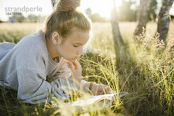 Mädchen liegt auf Gras und liest an einem sonnigen Tag ein Buch