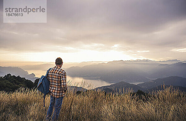 Reifer Mann mit Rucksack steht bei Sonnenuntergang auf dem Berg