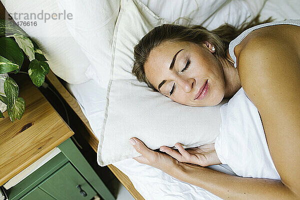 Woman with eyes closed relaxing in bed at home