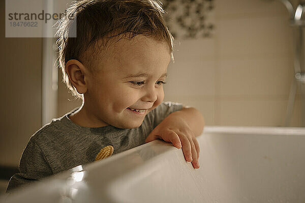 Lächelnder Junge steht am Waschbecken im Badezimmer