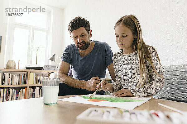 Vater sitzt neben Tochter und malt zu Hause auf Papier