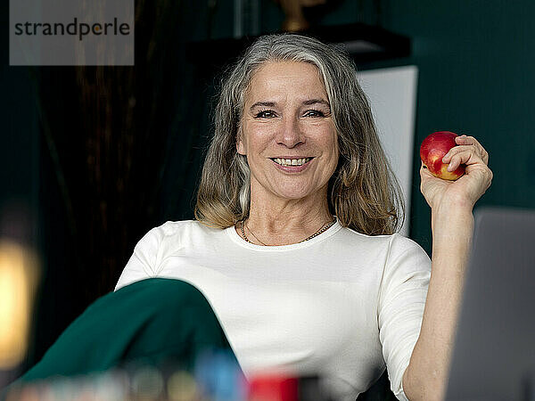 Glückliche Geschäftsfrau hält Apfel im Büro