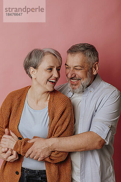 Happy mature couple enjoying together against pink background