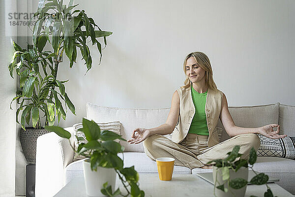 Lächelnde Frau praktiziert Meditation auf dem Sofa zu Hause