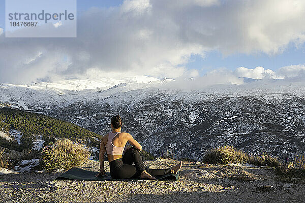 Frau macht Yoga auf einem Berg unter bewölktem Himmel