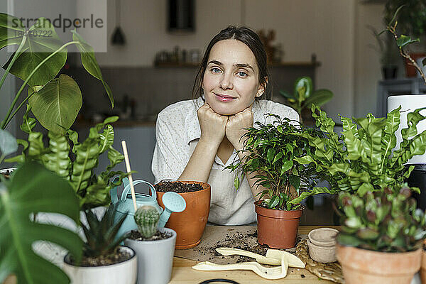 Lächelnde Frau stützt sich zu Hause auf Ellbogen an frische Pflanzen
