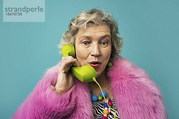 Senior woman talking on telephone against turquoise background