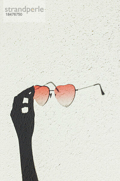 Schatten einer Hand  die eine herzförmige Sonnenbrille an der Wand hält