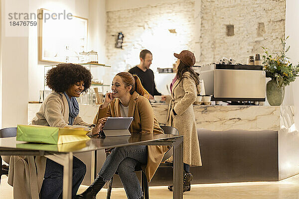 Glückliche junge Frau benutzt Tablet-PC mit Freund  der am Tisch im Café sitzt