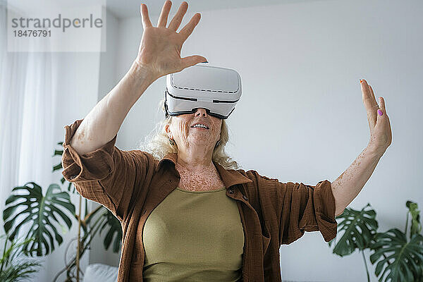 Ältere Frau mit Vitiligo-Haut trägt zu Hause ein Virtual-Reality-Headset