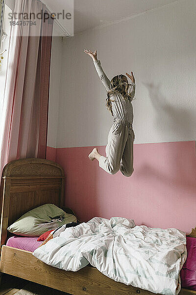 Carefree girl jumping on bed at home