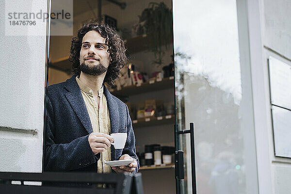 Nachdenklicher Geschäftsmann mit Kaffeetasse steht vor der Tür
