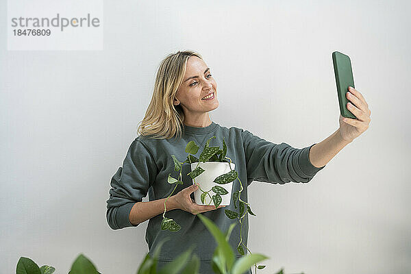 Lächelnde Frau macht zu Hause ein Selfie mit einer Topfpflanze