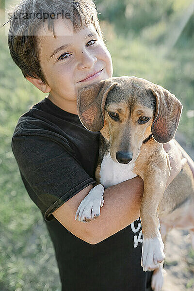 Netter lächelnder Junge  der einen braunen Outbred-Hund trägt