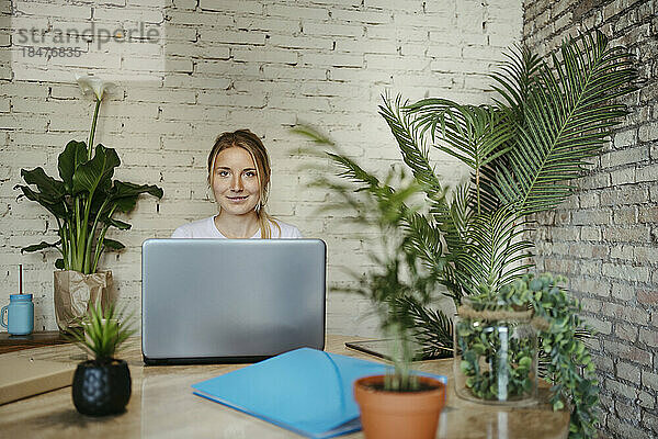 Lächelnde Geschäftsfrau hinter Laptop am Arbeitsplatz