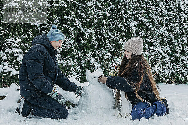 Lächelnde Freunde bauen im Winter im Park einen Schneemann