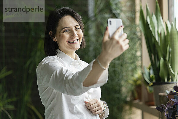 Glückliche Frau  die vor Pflanzen ein Selfie mit dem Smartphone macht