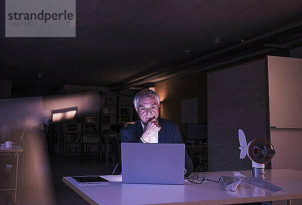 Geschäftsmann mit der Hand am Kinn arbeitet spät im Büro