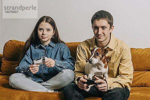 Lächelndes Teenager-Paar mit Hund spielt zu Hause Videospiel