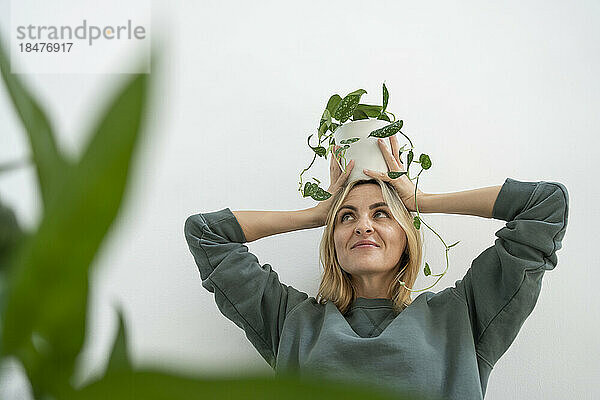 Smiling woman carrying plant on head in front of wall