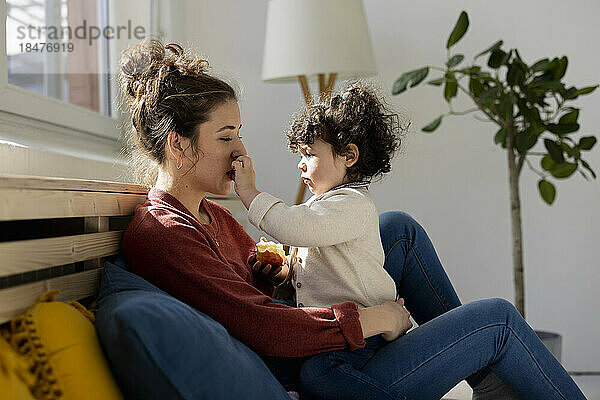 Daughter touching mother's face sitting on sofa