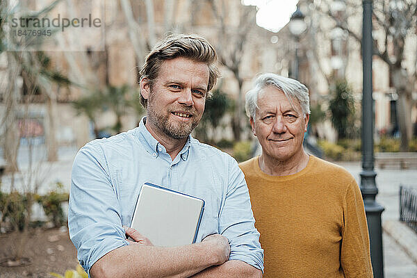 Happy man holding tablet PC and standing with father