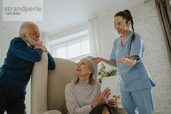 Fröhliche Krankenschwester gestikuliert von älteren Patienten zu Hause