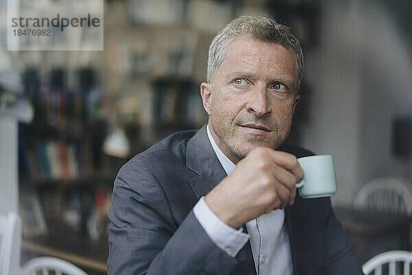 Thoughtful mature businessman with coffee cup seen through glass