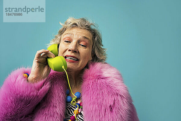 Frau im Pelzmantel telefoniert vor farbigem Hintergrund