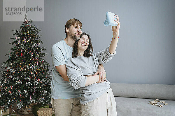 Lächelnde Frau macht zu Weihnachten zu Hause ein Selfie mit einem Mann mit einer Sofortbildkamera