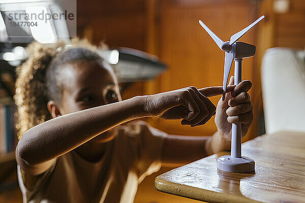 Mädchen rotierendes Rotorblatt eines Windturbinenmodells auf dem Tisch zu Hause
