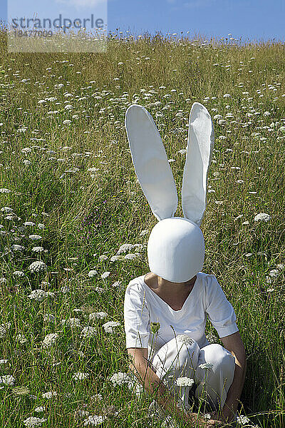 Woman with rabbit mask crouching in field