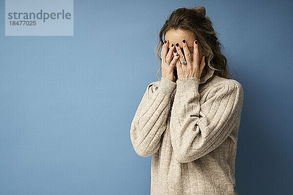 Woman covering face with hands against blue background