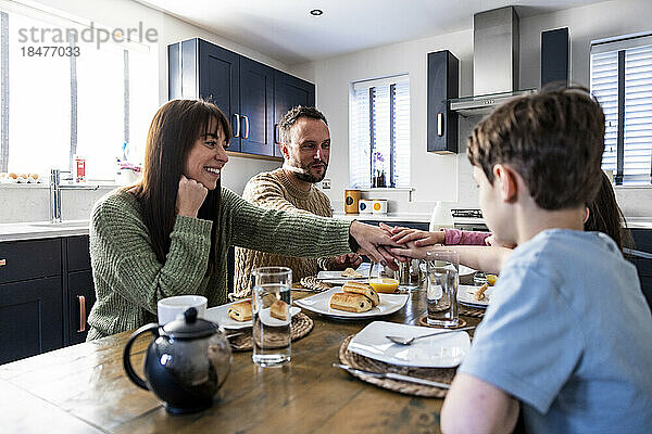 Glückliche Familie genießt gemeinsam das Frühstück mit gestapelten Händen am Tisch