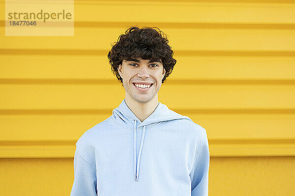 Glücklicher junger Mann mit Kapuzenshirt vor gelber Wand