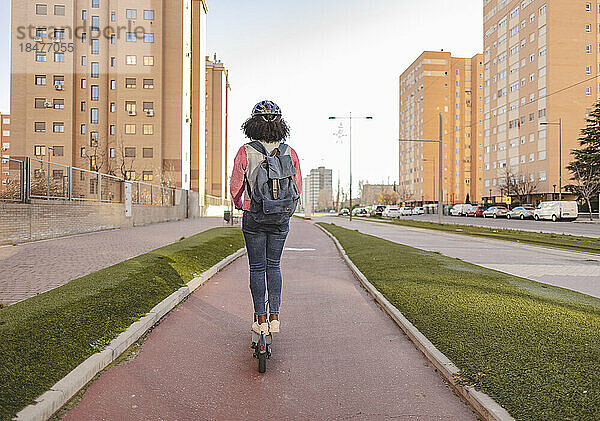 Junge Frau mit Rucksack fährt Elektroroller am Fußweg