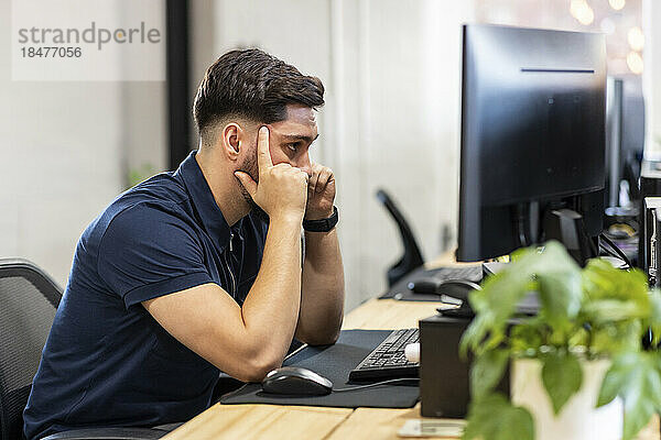 Frustrierter Geschäftsmann sitzt vor dem Desktop-PC im Büro