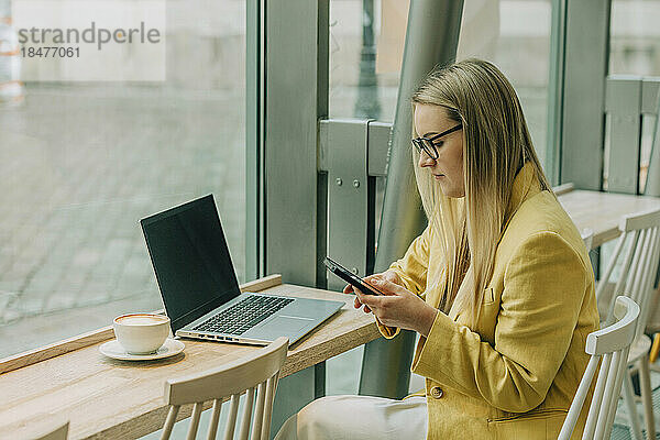 Geschäftsfrau benutzt Smartphone und Laptop am Tisch im Café