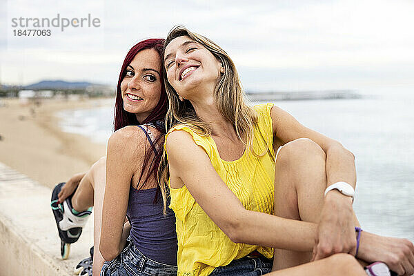 Glückliche Freunde sitzen Rücken an Rücken an der Promenade am Meer