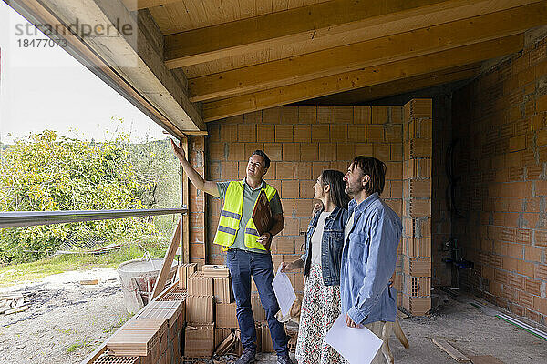 Glücklicher Bauunternehmer  der mit einem älteren Paar auf der Baustelle diskutiert