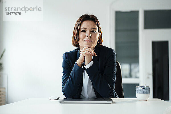 Junge Geschäftsfrau sitzt mit Laptop und Kaffee am Schreibtisch