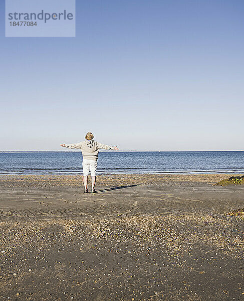 Ältere Frau bewundert an einem sonnigen Tag das Meer am Strand
